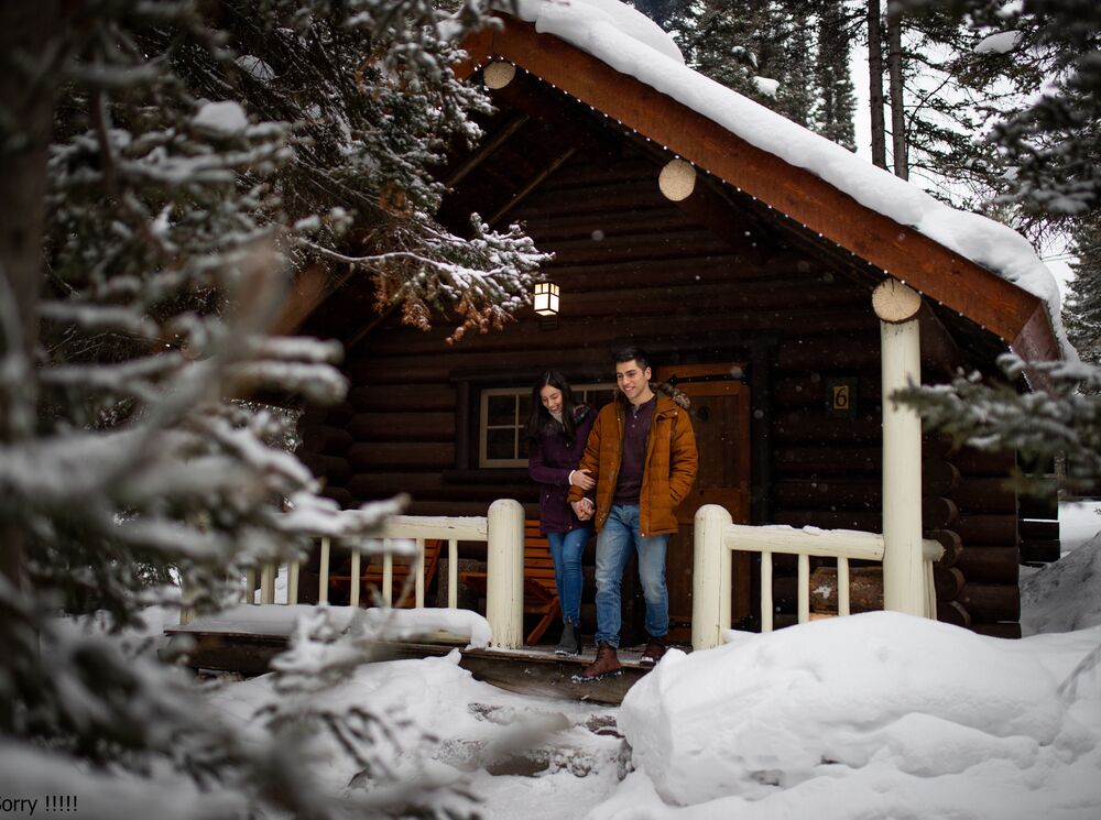 A couple walking out of a snowy cabin at Storm Mountain Lodge and Cabins in the winter in Banff National Park.